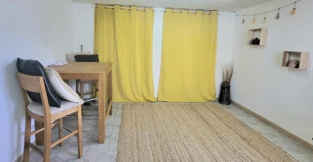 Cabinet de Guenrouët : table en bois et chaises devant deux rideaux jaunes