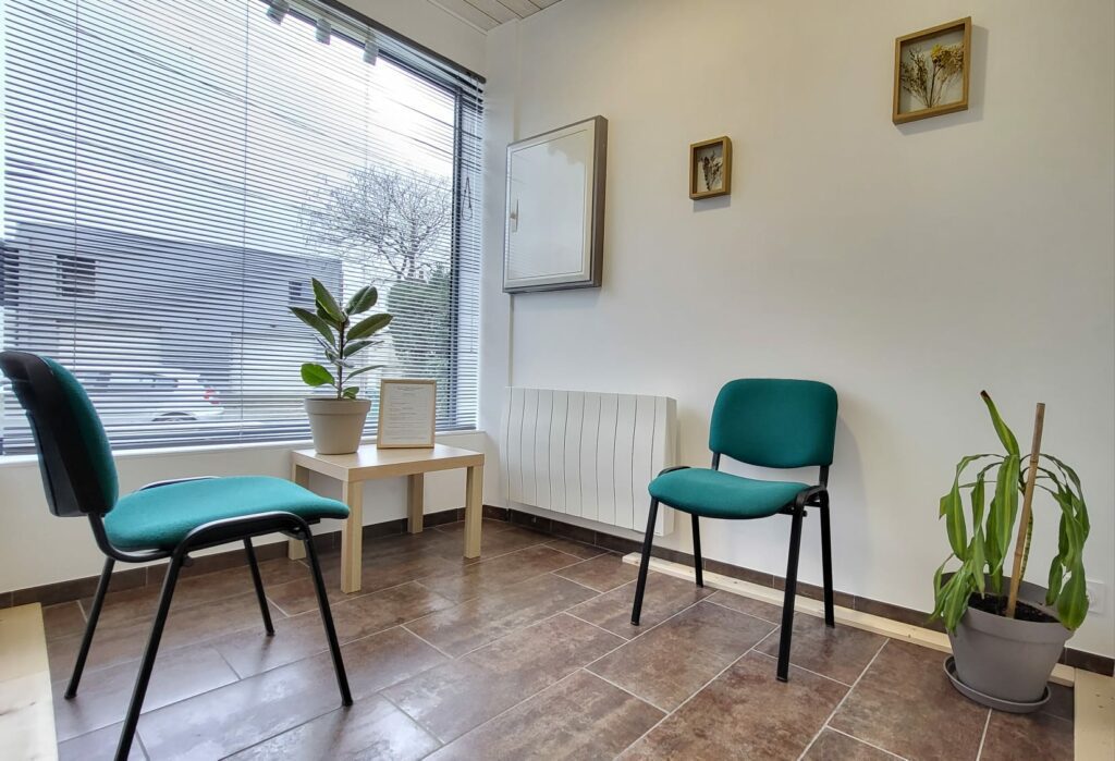 Salle d'attente du cabinet de Blain : deux chaises vertes, une petite table et des plantes devant la baie vitrée